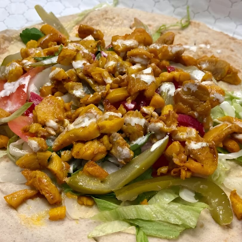 Close-up of a Grub Palace chicken wrap with lettuce, tomatoes, onions, pickles, and white sauce.