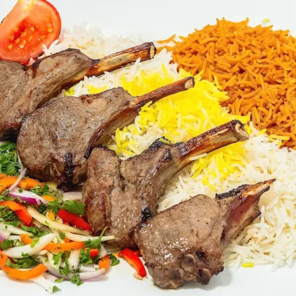 Grilled lamb chops with white, yellow, and orange rice, fresh salad, and a tomato slice.