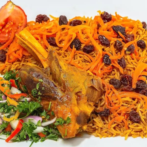 Afghan lamb shank with seasoned rice, shredded carrots, raisins, and a side salad.