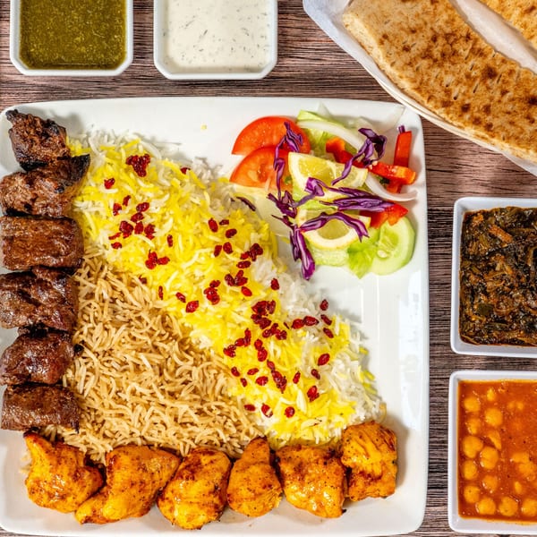 A large platter of Persian food with two types of rice, two skewers of meat, and a side salad.