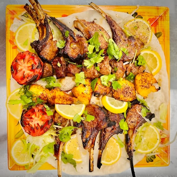 Grilled lamb chops, chicken, and beef kebabs with roasted tomatoes, lemons, and cilantro on a platter.