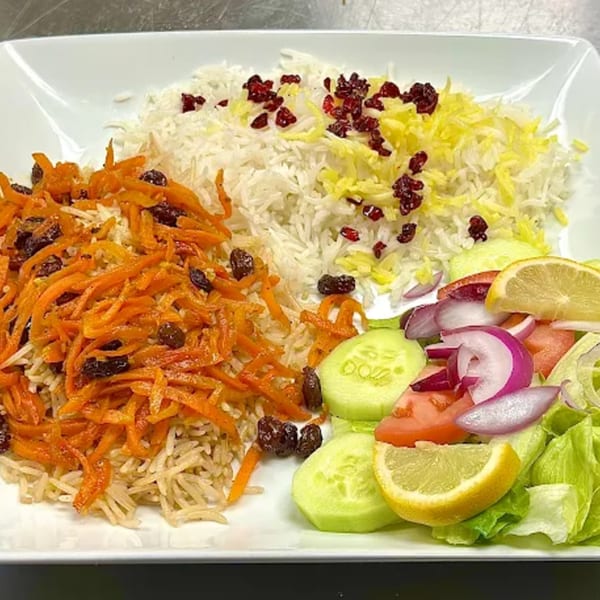 Platter of Afghan rice with shredded carrots, raisins, and a side salad with lemon.